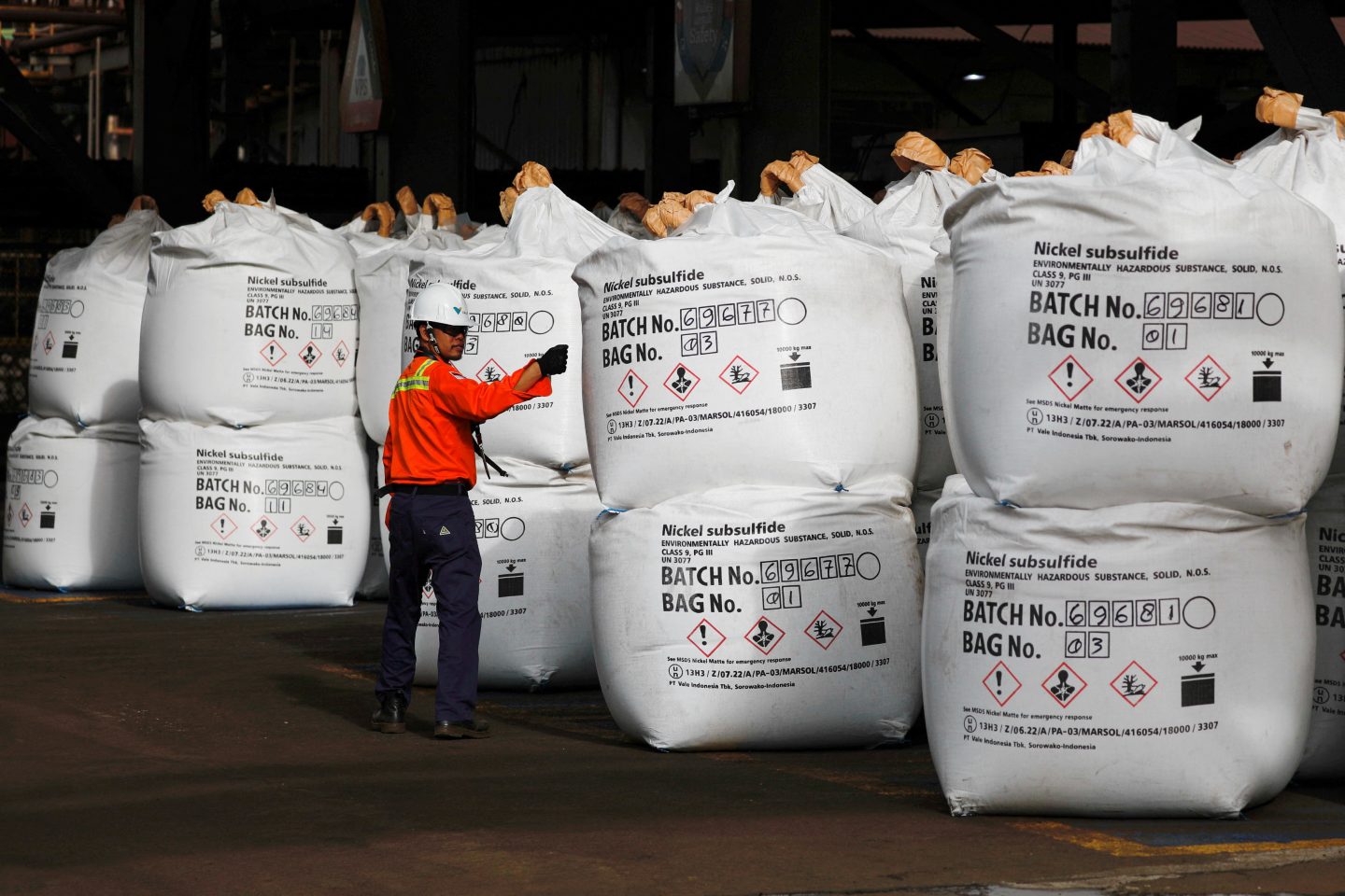 A worker in a hard hat and red jacket inspects large bags of nickel subsulfide at a nickel smelter in Sorowako, South Sulawesi province, Indonesia